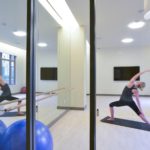 A person is doing yoga in a well-lit studio with mirrors, exercise balls, and a barre, situated in one of the modern Navy Yard apartments. They are in a side-angle pose on a yoga mat.