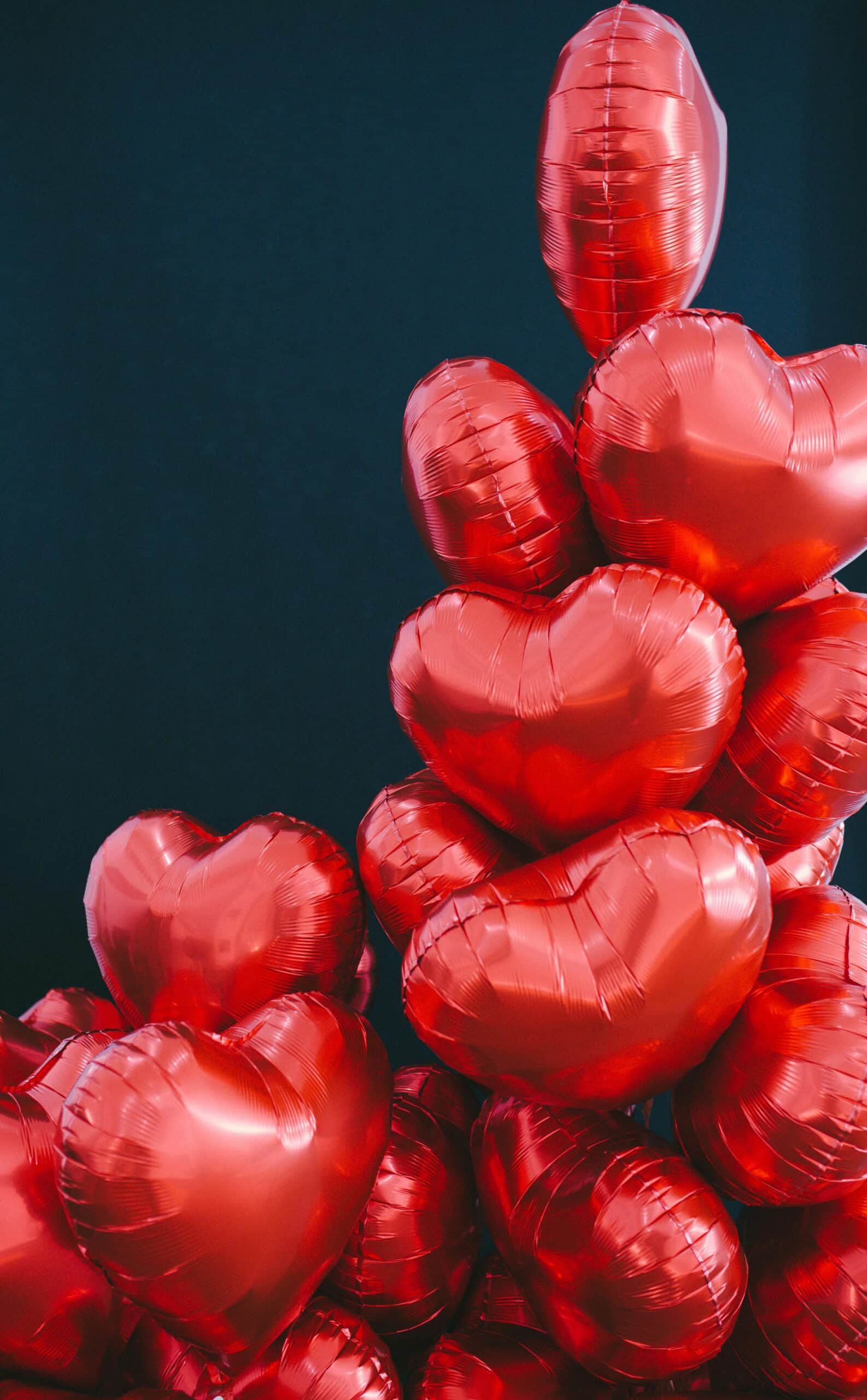 A pile of red, heart-shaped balloons against a dark blue background.