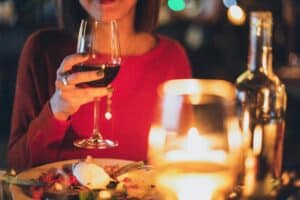 Person holding a glass of red wine at a candlelit dinner table, with a blurred background.